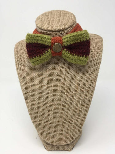 Hand-knitted green, burgandy, and orange pet bow tie on a tan brown bust
