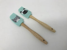 Load image into Gallery viewer, Pair of wooden handle spatulas with turquoise green heads featuring cats on them laying flat on a white surface 

