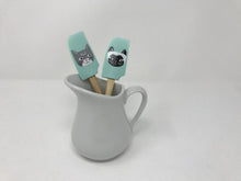 Load image into Gallery viewer, Pair of wooden handle spatulas with turquoise green heads featuring cats on them inside of a white gravy boat 
