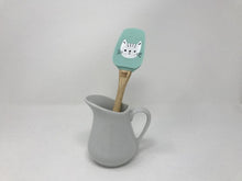 Load image into Gallery viewer, Wooden handled spatula with a turquoise green head featuring a white cat on it inside of a white tea cup
