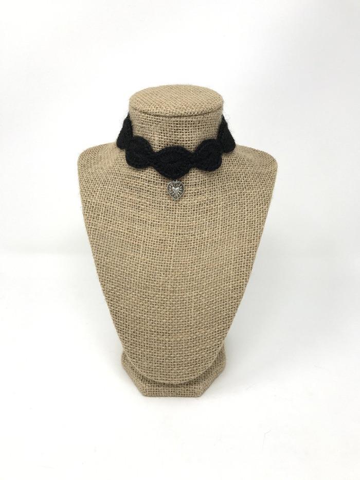 Picture of a black hand-knitted cat collar with silver charm around a brown bust of a neck