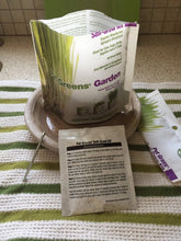Load image into Gallery viewer, A picture of an open bag of pet greens self-grow kit standing on a circular plant dish 

