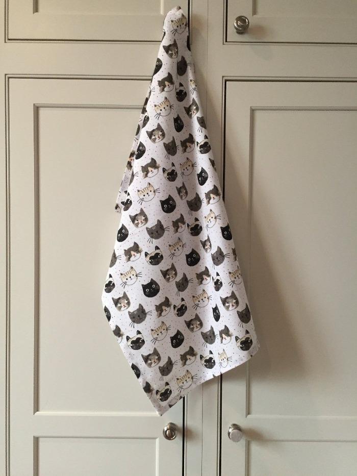 White cat-themed kitchen towel hanging from a kitchen cupboard handle