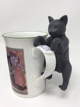Load image into Gallery viewer, Black cat-themed tea infuser hanging on the side of a teacup 

