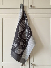 Load image into Gallery viewer, Picture of a black and white cat-themed kitchen towel hanging from a white kitchen cupboard handle 
