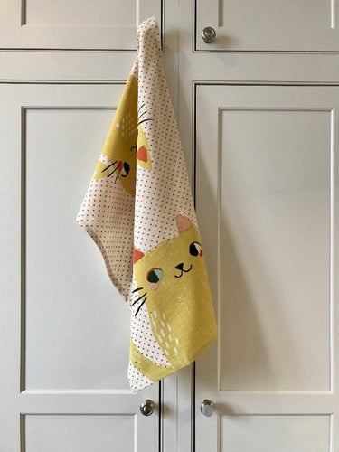 White kitchen towel with red dots and two big yellow cats on it hanging from a white kitchen cupboard