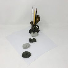 Load image into Gallery viewer, Two black and two grey cat shaped erasers laying flat on an all white surface with a brass colored pen holder with pens and pencils in it
